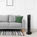 A grey couch with a black VisionAir oscillating tower fan next to it.