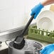 A person in blue gloves cleaning a pot with an Advantage Supplies black floating utility/pot scrub brush.