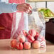 A person holding a white polypropylene soft loop handled bag of red apples.