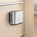 A silver and black rectangular Tork stainless steel double jumbo roll toilet paper dispenser on a wall.