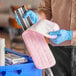 A person wearing blue gloves using a pink and white Advantage Supplies microfiber mop pad to clean a rectangular object.