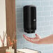 A person using a Tork black wall-mount automatic foam hand soap dispenser.