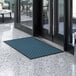 A blue and black Lavex Parquet entrance mat on a tiled floor in front of a glass door.