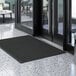 A Lavex black entrance mat on a marble floor in front of a glass door.
