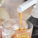 A person pouring Capora Caramel Flavoring Sauce into a glass with ice.