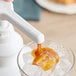 A person pouring Capora caramel sauce into a glass of ice.