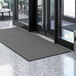 A black Lavex parquet entrance mat with a gray pattern on a marble floor.