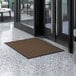 A brown Lavex parquet entrance mat on a white tiled floor next to a glass door.