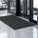 A black Lavex Needle Rib entrance mat on a marble floor.