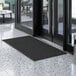 A black Lavex Needle Rib entrance mat in front of a glass door.