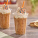 A plastic cup of iced coffee topped with whipped cream and a decorated cookie, featuring a pumpkin spice theme.