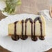 A slice of cheesecake on a white plate with Capora chocolate sauce drizzled on top.