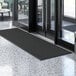 A black Lavex Needle Rib indoor entrance mat in front of a glass door.