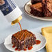 A brownie on a white plate with Capora salted caramel sauce drizzled on top.