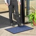 A man standing on a blue Lavex waffle entrance mat holding a book.