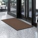 A brown Lavex Needle Rib entrance mat in front of glass doors.