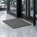 A gray Lavex parquet entrance mat on a white marble floor in front of a glass door.