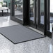 A grey rectangular Lavex indoor entrance mat placed in front of a door.