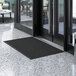 A black Lavex Needle Rib entrance mat in front of a glass door.