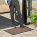 A man in a suit standing on a Lavex brown indoor entrance mat holding a book.