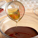 A person pours Malt Products Organic Agave Syrup into a bowl of chocolate in a home kitchen.