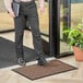 A man standing in front of a door with a brown Lavex Water Absorbent Parquet entrance mat.