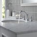 A marble bathroom counter with a Delta Woodhurst widespread deck-mount faucet running water.