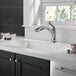 A kitchen sink with a Delta deck-mount kitchen faucet and a window.