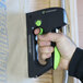 A hand using a green and black Surebonder TriggerFire staple gun on a piece of wood.