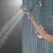 A hand holding a Delta stainless steel 2-in-1 hand shower and showerhead.