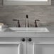 A white surface with a Delta Venetian Bronze Woodhurst widespread deck-mount lavatory faucet with lever handles and a pop-up drain.