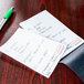 A table in a pizza parlor with a white guest check with writing next to a pen.