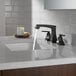 A white sink with a Delta Ashlyn widespread deck-mount faucet running water.