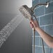 A hand holding a Delta stainless steel 2-in-1 shower head.