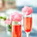 Two glasses of red liquid with pink cotton candy on top.