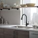 A Delta Essa matte black kitchen faucet with a lever handle and pull-down spray wand over a kitchen sink with a window above it.