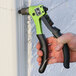 A hand using a Surebonder Heavy-Duty Professional Compact Rivet Tool with black and green handles to install a rivet.