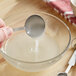 A person using a spoon to mix Nuvert Congealed Invert Syrup into a glass bowl.