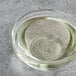 A clear glass bowl of Nuvert Medium Invert Syrup over a white surface with a drop of syrup in it.