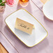 A Visions white rectangular plastic coupe platter with a gold place card on it.
