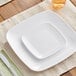 A white Visions square plastic coupe plate with a knife and fork on a table.