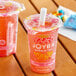 Two plastic cups of Joyba strawberry lemonade green bubble tea on a table.