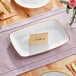 A table setting with a Visions white rectangular plastic platter with a place card on it.