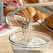 A person pouring TapRite Tapioca Syrup into a bowl of white powder.