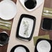 A table with white square plastic plates with silver borders and silverware.