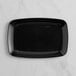 A black rectangular Visions plastic serving tray on a white marble surface.