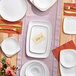 A table set with Visions white square plastic plates with gold rims and silverware.