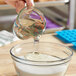 A hand pouring clear Malt Products RiceRite Rice Syrup into a bowl.