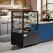 A black Avantco refrigerated bakery display case with cakes inside.