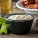 A bowl of white sauce with celery sticks in a Carlisle black fluted ramekin.
